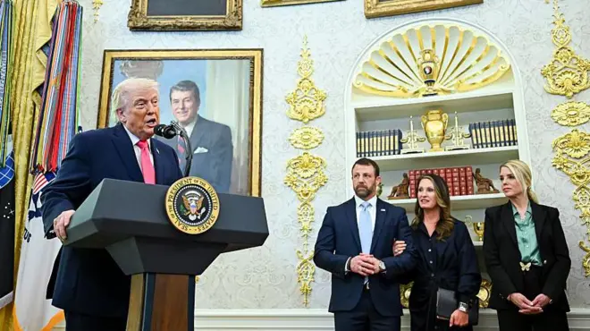 Trump kürsüde sağında bir erkek iki kadın ayakta bekliyor hepsi resmi giyimli. 