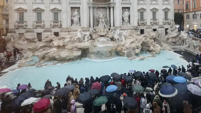 фонтан треви в окружении туристов, многие из них с зонтами