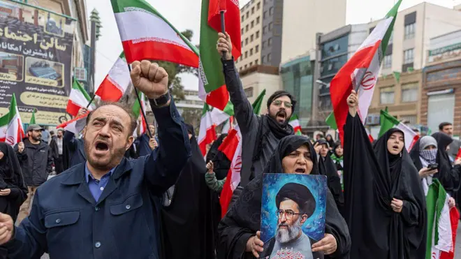 Grupo de manifestantes em Teerã, no Irã, contra os ataques dos Estados Unidos e Israel, gritando com os punhos erguidos