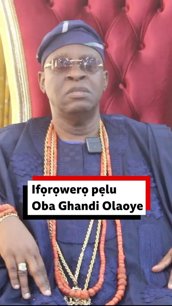 Sọun tilẹ Ogbomoso, ọba Ghandi Olaoye wọ asọ oke olomi aro to jẹ agbada, sokoto ati fila. O fi ọpọ ilẹsẹ sọrun ati ọwọ, ati igo dudu soju, joko apere, o n wo ọkankan.