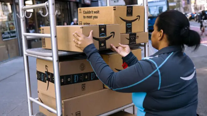 Una trabajadora de Amazon apila paquetes en un carrito frente a un edificio de apartamentos en Nueva York.