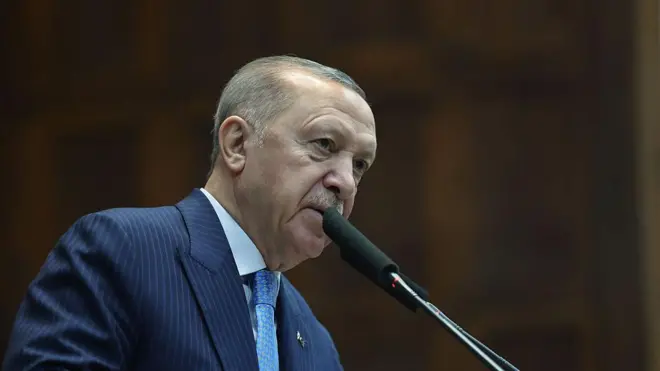 Lacivert çizgili takım elbise giymiş bir adam kürsüde konuşuyor