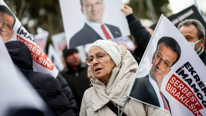 9 Mart 2026, bir kadın İmamoğlu serbest bırakılsın yazılı bayrak tutuyor, protestocularla birlikte.