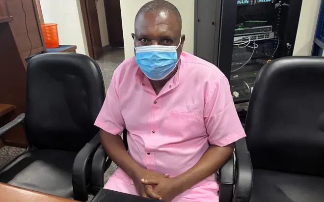 Vincent Murekezi yicaye yambaye agapfukamunwa n'imyenda y'iroza y'imfungwa zitarakatirwa bidasubirwaho n'inkiko zo mu Rwanda