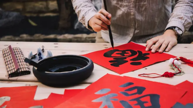 有人在木桌上的紅色方形揮春上以毛筆書寫漢字。