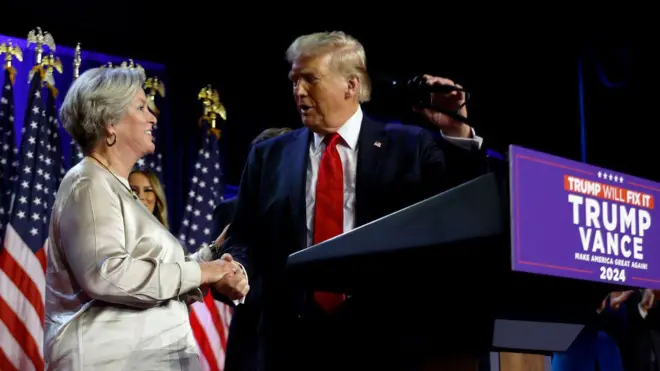Donald Trump wit red tie and Susan Wiles facing each oda for stage