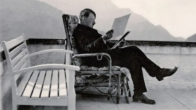 Adolf Hitler sentado em uma cadeira na varanda lendo documentos