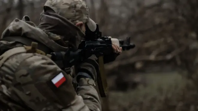 Żołnierz w kamuflażu z polską flagą na ramieniu i z karabinem szturmowym 