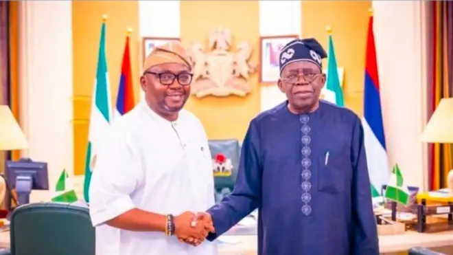 Adebayo Adelabu wọ aṣọ buba funfun pẹlu fila, o ba Aarẹ Bola Tinubu lọwọ, aarẹ naa wọ aṣọ buba buluu pẹlu fila