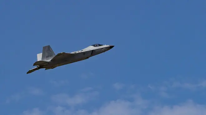 青空を背景に、灰色の戦闘機が左から右へと飛んでいる