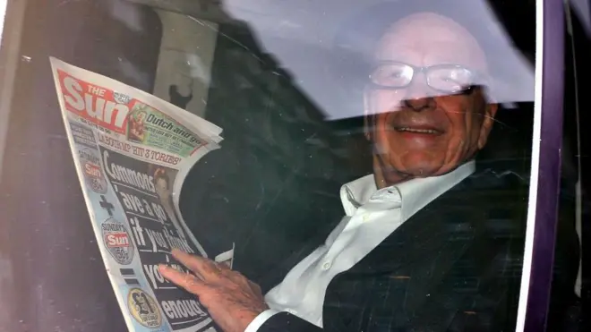 مرداک در خودرو در حالیکه روزنامه سان در دست گرفته و می‌خندد