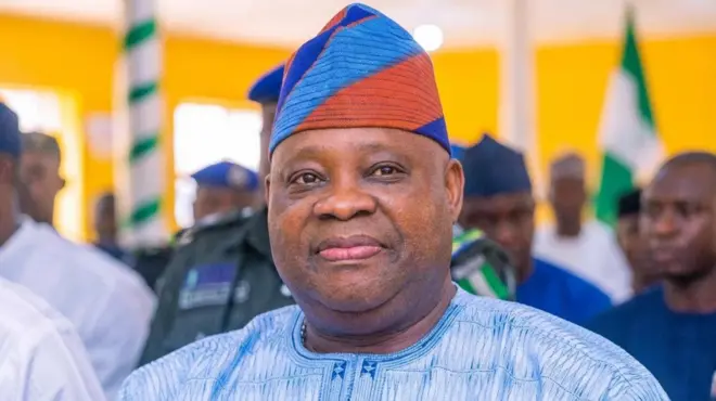Gomina Ademola Adeleke, o wọṣọ alawọ aro, o de fila alawọ kan naa to ni pupa ninu. O n rẹrin-in muse ninu aworan yii.