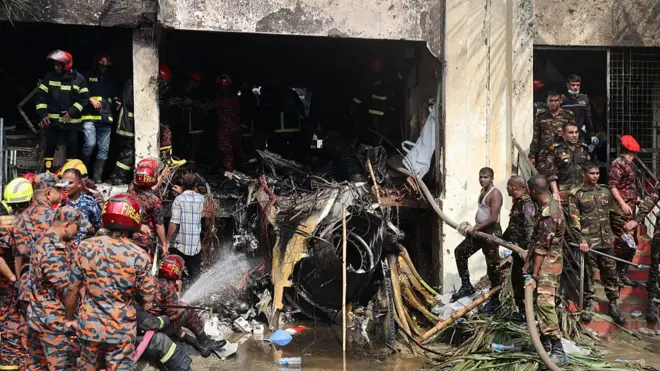 The charred fuselage can be seen inside the building, with wreckage all around and many emergency service workers in bright red and orange work suits