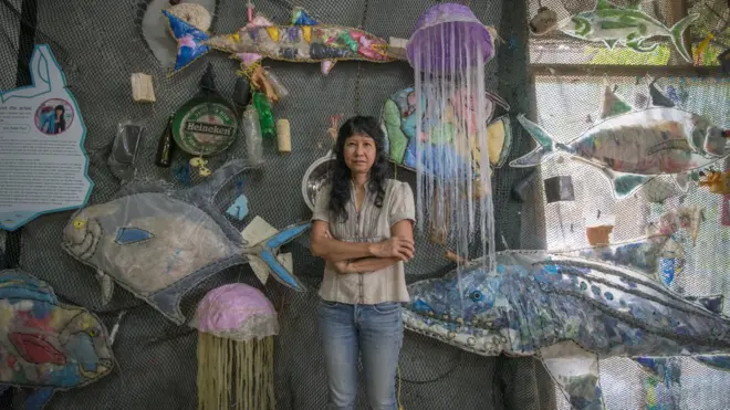 อาจารย์ป้อม-ประสพสุข เลิศวิริยะปิติ ยืนอยู่ท่ามกลางงานศิลปะ จำลองท้องทะเลที่เต็มไปด้วยฝูงปลาที่กลืนพลาสติกเข้าไป