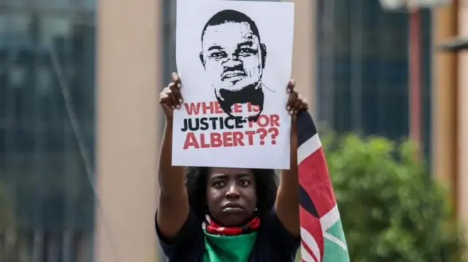 One protester wey wrap Kenyan flag for im body hold one foto of Albert Ojwang wit di words 'Where is justice for Albert??'