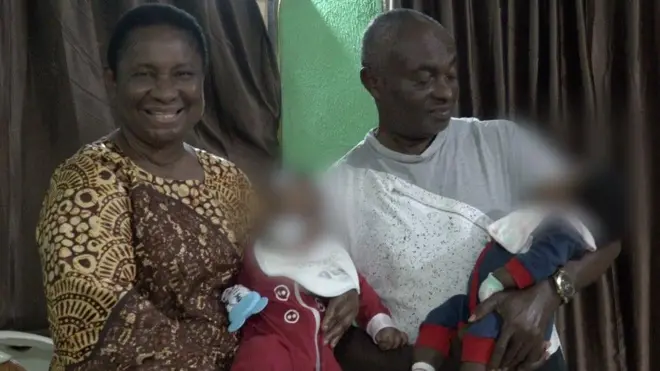 Pasitọ Olufunmilola to wọn ankara olomi Kọfi ati goolu n rẹrin pẹlu ọkọ rẹ, Emmanuel to wọ asọ oyinbo funfun, ni ikọọkan wọn gbe awọn ibeji lọwọ.