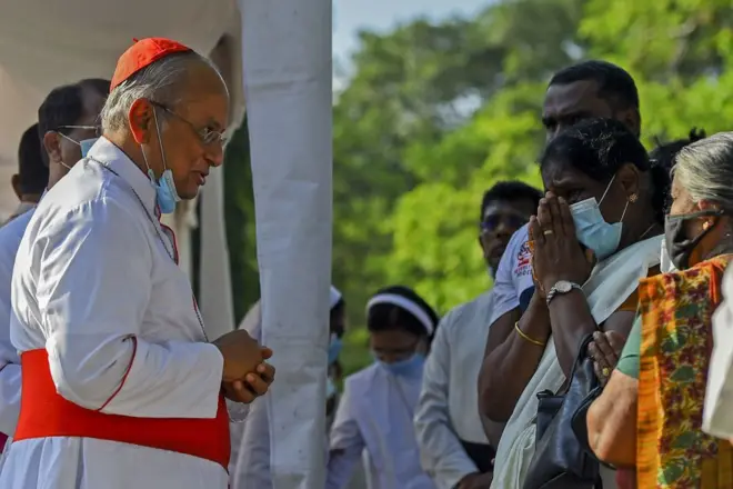 The head of the Roman Catholic church in Sri Lanka, Cardinal Malcolm Ranjith (L) speaks with people at a memorial in the main cemetery in Colombo on April 18, 2021, after he opened monuments to commemorate the 279 people killed in the 2019 Easter Sunday attacks