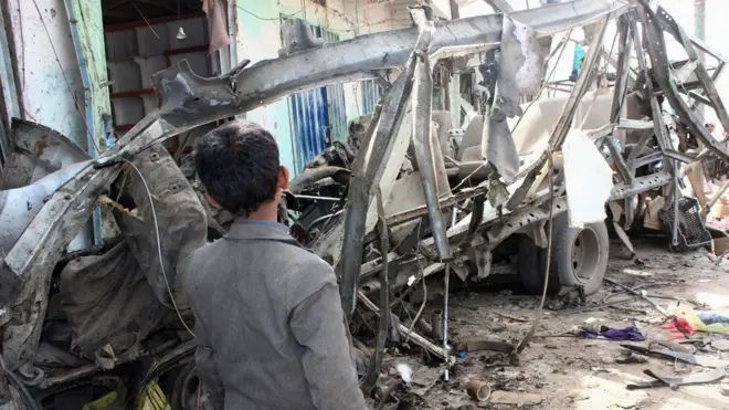 طفل يمني يقف بجانب بقايا حافلة مدرسية قصفتها طائرات التحالف في صعدة أوائل الشهر الحالي
