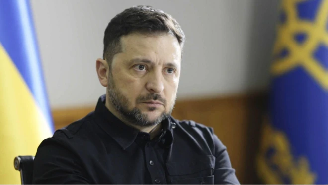 Zelenskiy karşıdaki muhabire bakıyor. Arkada Ukrayna bayrakları var.