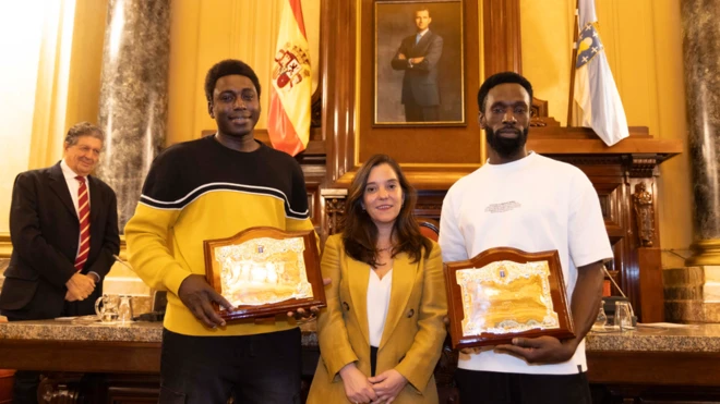 (de gauche à droite) Magatte N'Diaye, Inés Rey et Ibrahima Diack dans la salle du conseil municipal. Les hommes tenant leur plaque se tiennent de part et d'autre du maire.