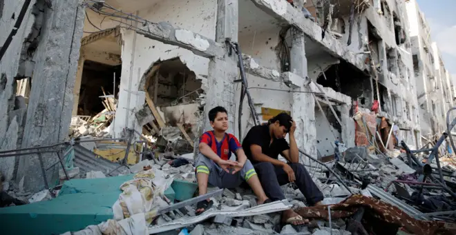 طفلين من غزة يجلسان أمام بيتهما المدمر