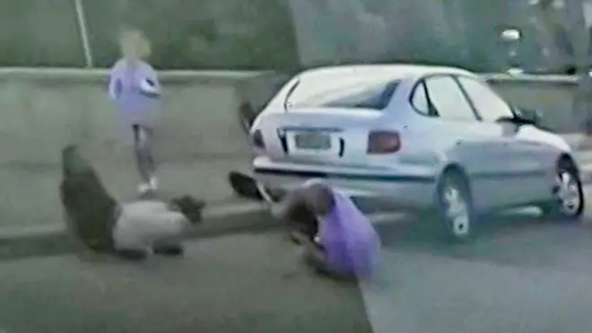 画質の粗いドライブレコーダーの映像の静止画。道端で2人の男性が銃を奪い合っている様子が映っている。一人は黒い服、もう一人は紫の服を着ている。