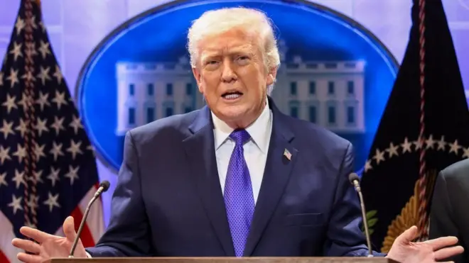 ダークスーツに青いネクタイを着けたトランプ氏が、ホワイトハウスでの記者会見で、両手を広げて話している。後ろには星条旗が置かれ、壁にはホワイトハウスのイラストがある