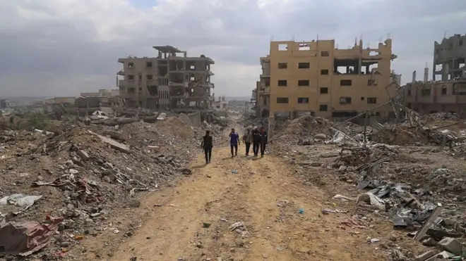 چند مرد در مسیری خاکی بین ویرانه های غزه قدم می‌زنند