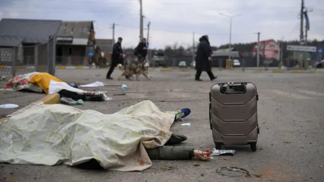 Dos cuerpos cubiertos con telas en la carretera de Irpín, junto a maletas y otras personas escapando de la ciudad.