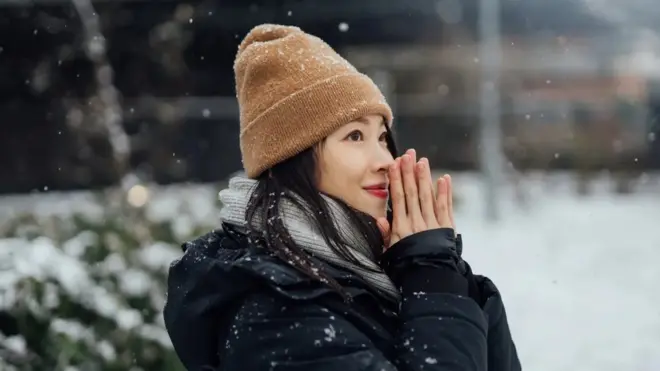 두 손을 모으고 눈을 맞고 있는 여성