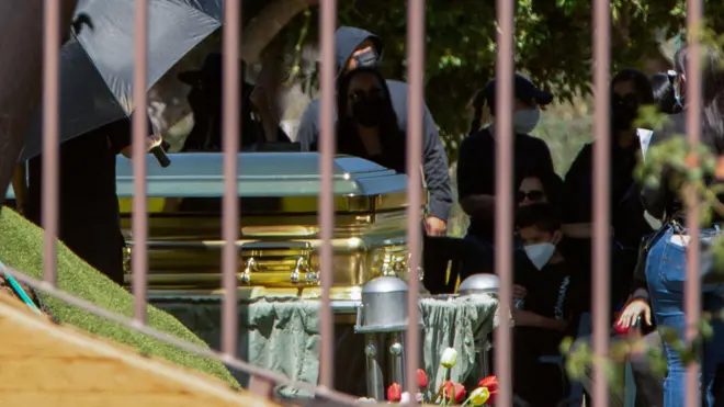 Золотой гроб и люди в масках на похоронах Эль Менчо. Фото сделано сквозь решетку ограды