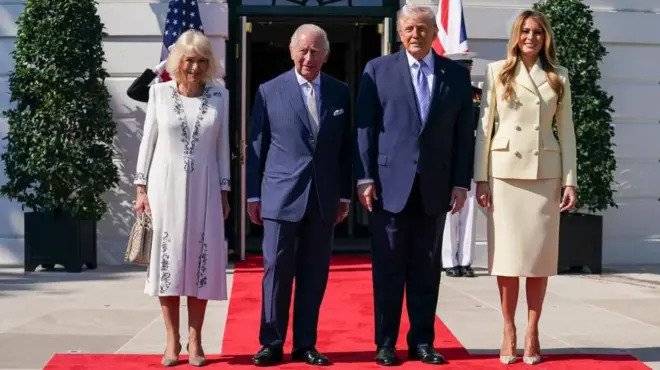 アメリカとイギリスの両国国旗が左右に立つドアを前に、赤じゅうたんの上に並ぶ（左から）カミラ王妃、チャールズ国王、トランプ大統領、メラニア夫人