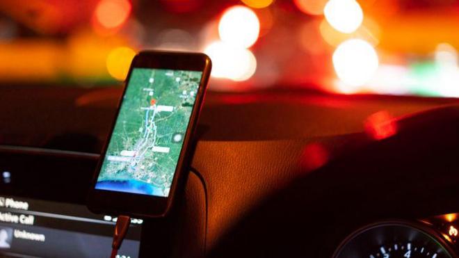 celular, apoiado em painel de um carro, com mapa de navegação aberto. ao fundo, luzes de trânsito
