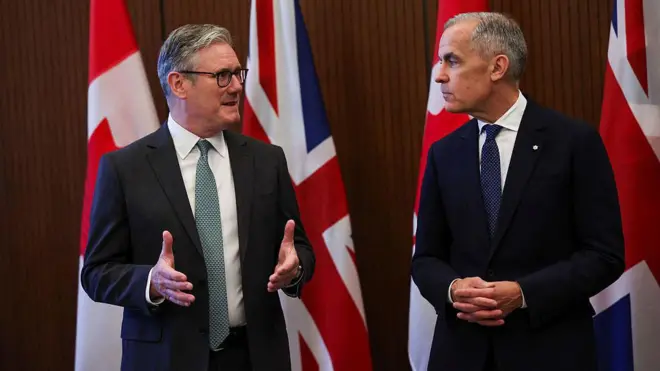 Canada Prime Minister Mark Carney on di left wearing black suit, white shirt and tie and Britain Prime Minister Keir Starmer wearing black suit and white shirt wit ash-coloured tie, dem meet bifor di start of di G7 summit onn June 15, 2025 for Canada.