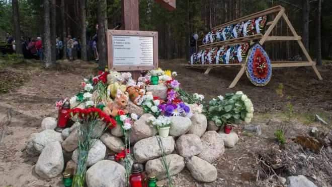 Игрушки и венки у подножия деревянного креста