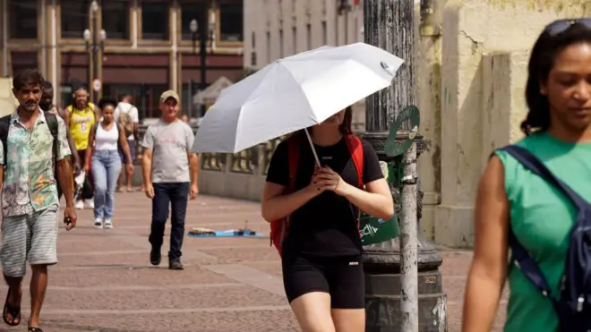 Pessoas caminham na rua durante ondabetano app downloadcalorbetano app downloadSão Paulo. Uma delas usa um guarda-chuva para se proteger do sol