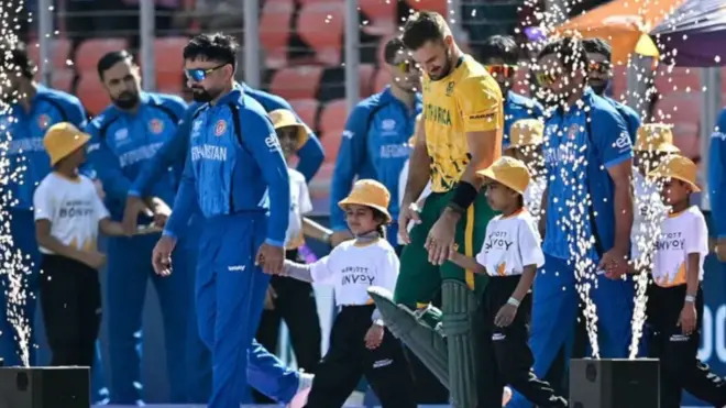 تصویری از افتتاحیه بازی هنگامی که بازیکن‌ها وارد میدان می‌شوند. کپتان‌های افغانستان و افریقای جنوبی در حالی دیده می‌شوند که دست کودکان را هنگام وارد شدن به میدان به دست دارند تا مراسم پیش از بازی را آغاز کنند.