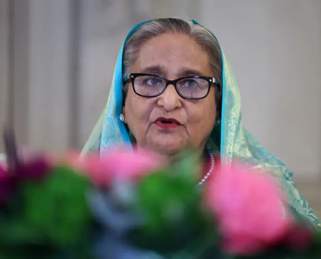 شیخ حسینه، رهبر پیشین بنگله‌دیش. زنی سالخورده که عینک به چشم دارد و چادری زمردی به سر.