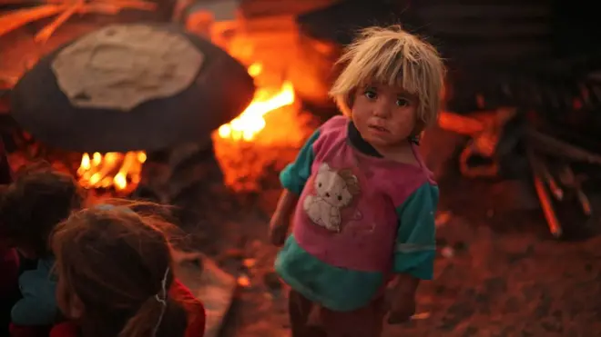 A Syrian child stands next to a bread-baking pit at the Ash'ari camp for the displaced in the rebel-held eastern Ghouta area outside the capital Damascus on October 25, 2017. / AFP PHOTO / Amer ALMOHIBANY