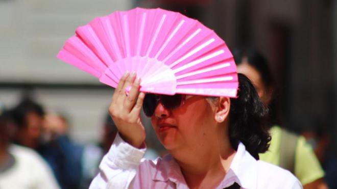 Una mujer se protege con un abanico del sol