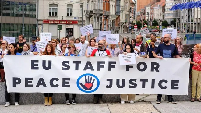موظفون حكوميون من الاتحاد الأوروبي يحملون لافتة كبيرة مكتوب عليها "موظفو الاتحاد الأوروبي من أجل السلام والعدالة"، يتظاهرون بأدوات المطبخ بين مبنى بيرلايمونت وأوروبا، في قلب الحي الأوروبي في بروكسل- بلجيكا. 