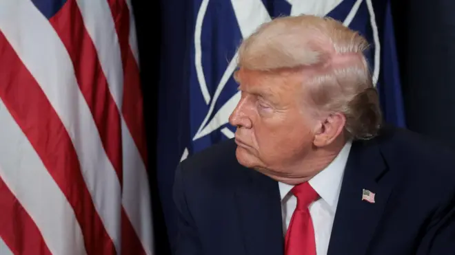 नेटोको महासचिव मार्क रुटसँगको बैठकमा सहभागीहुँदै अमेरिकी राष्ट्रपति ट्रम्प। निलो कोट, सेतो सर्ट र कलेजी टाइ लगाएका उनको पृष्ठभूमीमा अमेरिकी झन्डा देख्नसकिन्छ।