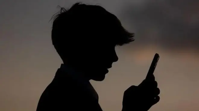 پرهیب یک پسر نوجوان که موبایلی در دست نگاه می‌کند