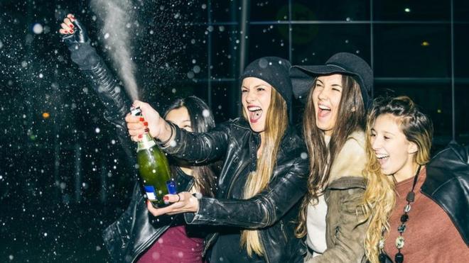 Cuatro mujeres descorchando una botella de champagne.