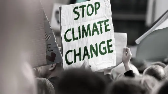 تجمعی در اعتراض به تخریب محیط‌زیستی، فردی نوشته‌ «تغییرات اقلیمی را متوقف کنید» در دست گرفته