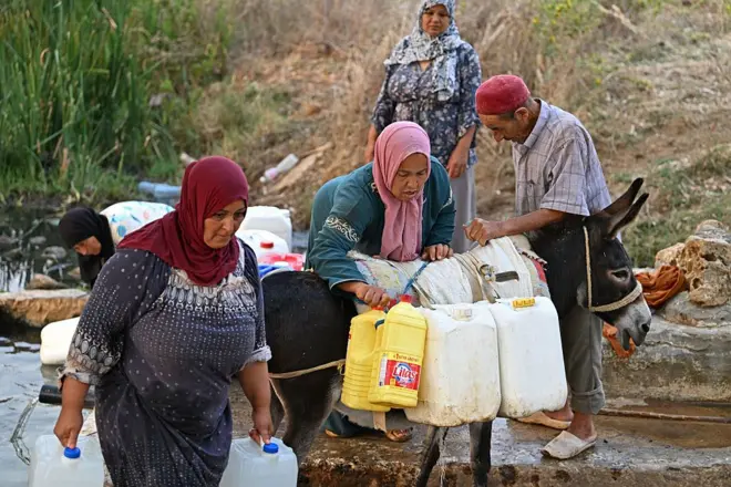 امرأة تحمل حاويات على ظهر حمار بعد جلب الماء من نبع طبيعي في يوم حار بجبال بنزرت