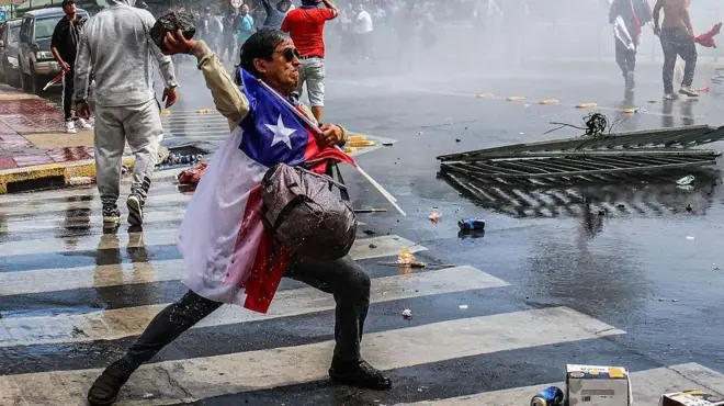 Protestas sociales de pescadores en Chile. Un trabajador cubierto con la bandera chilena lanza una piedra grande a la policía 