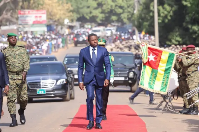 Faure Gnassingbé, le chef de l'Etat togolais passant en revue une troupe avec des véhicules en arrière-plan