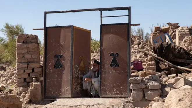 A man sitting at a doorway - the only remaining piece of what used to be his home