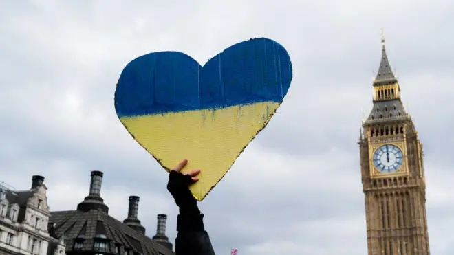 Табличка в форме сердца в цветах украинского флага, поднятая на фоне Биг-Бена